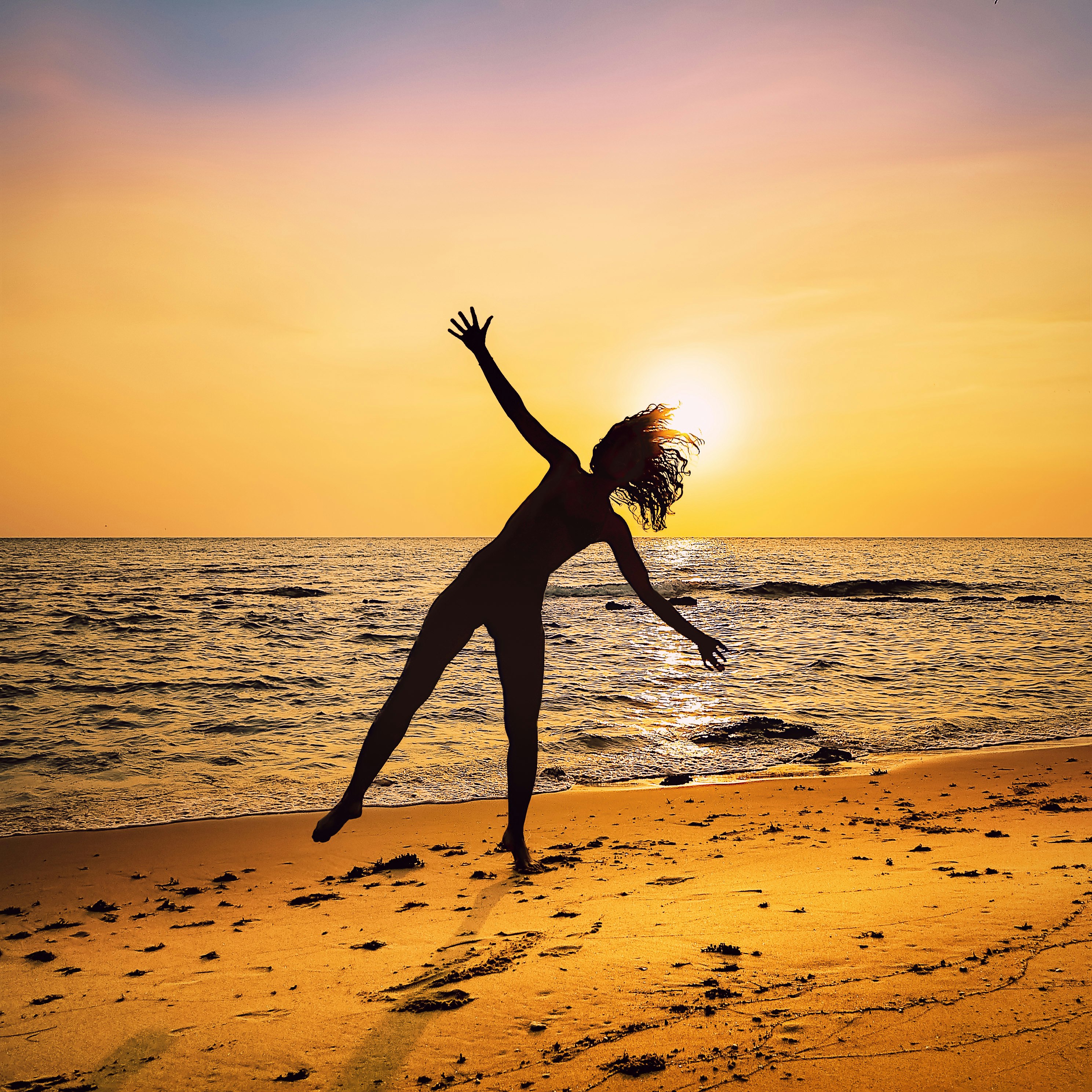 A woman about to do a cartwheel on the beach.